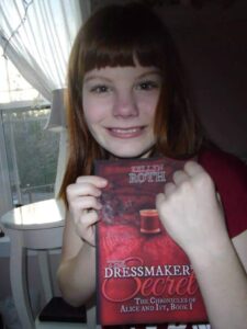 A girl holding up a book with red hair.